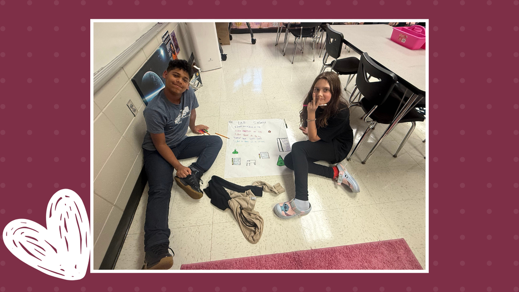 There is a boy and a girl on the floor working together on the Science Lab Safety Poster