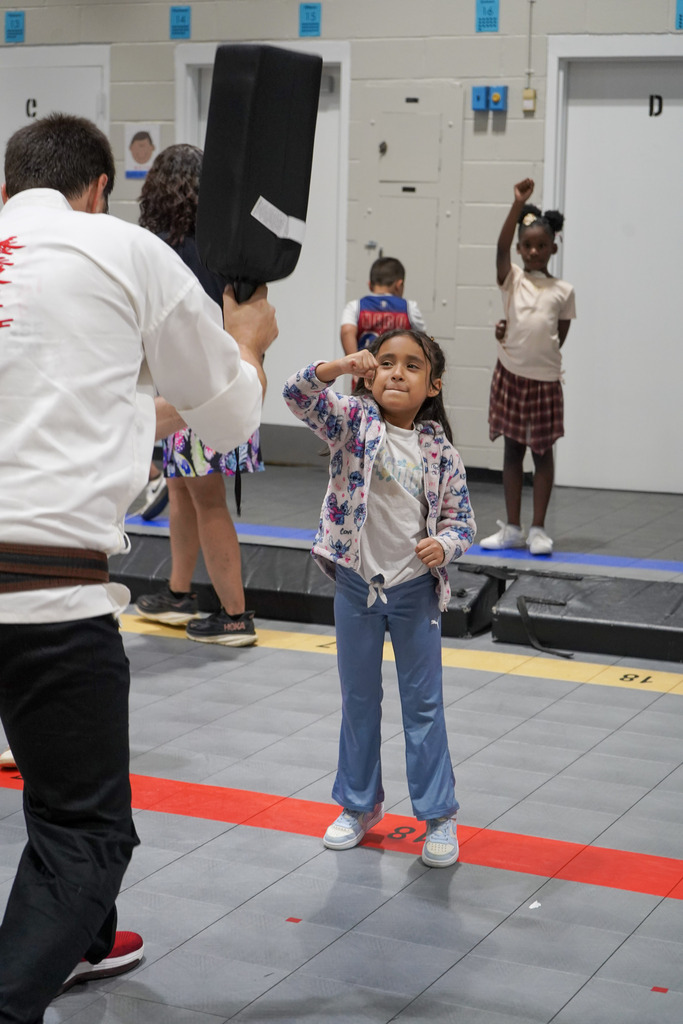 A student blocks a strike from a karate instructor during a lesson in a school gym.