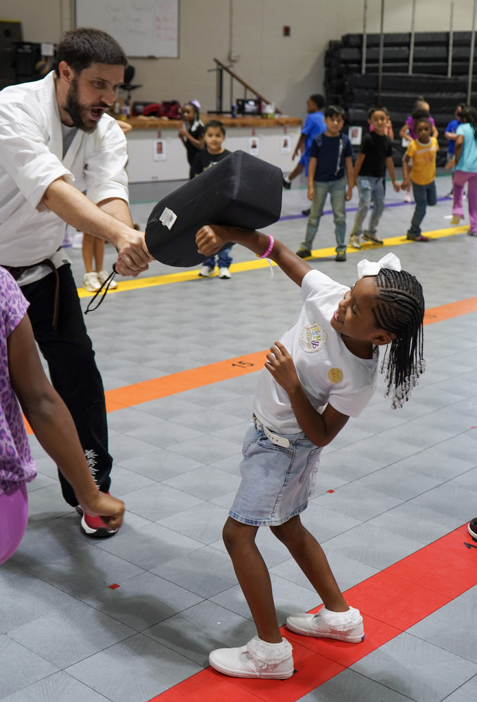 A child blocks a strike from a karate instructor inside a school gym.
