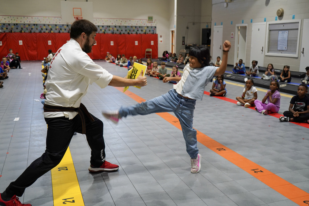 A student breaks a board being held by a karate instructor inside a school gym.