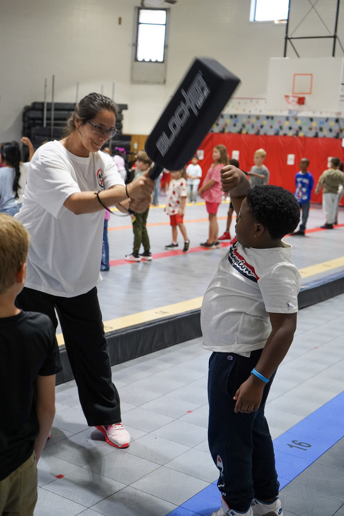 A child blocks a hit from a karate instructor inside a school gym.