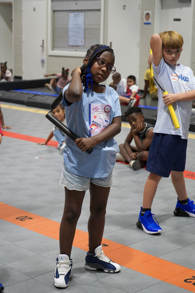 Children hold nunchucks in their hands while standing in a school gym.