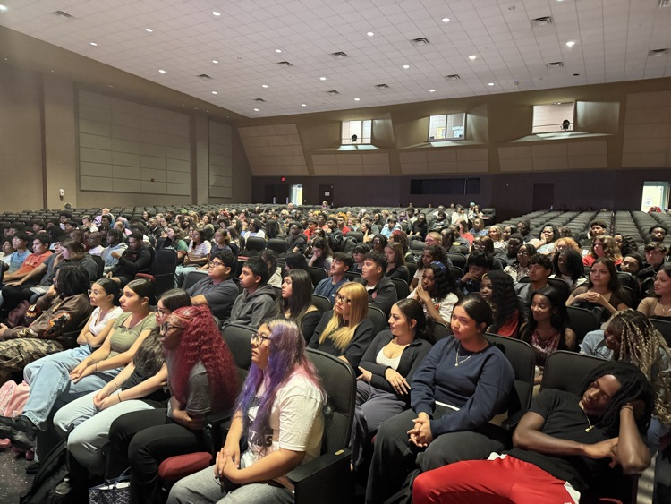 a large group of students listens to a presentation from their seats in the auditorium