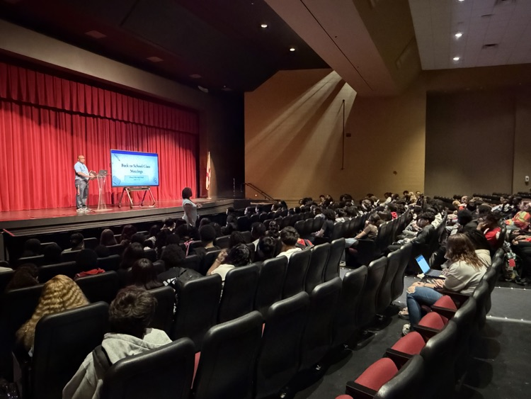 a large group of students listens to a presentation from their seats in the auditorium