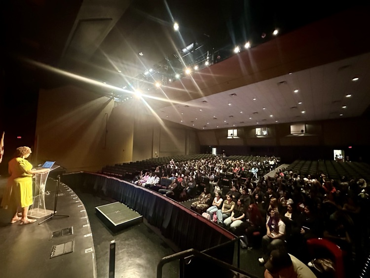a large group of students listens to a presentation from their seats in the auditorium
