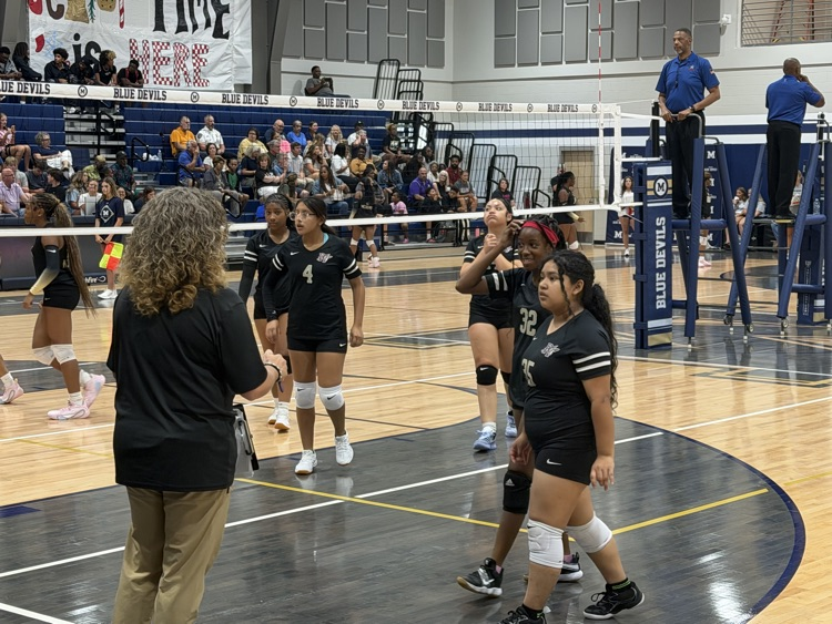 the jv volleyball team meets with the coach on the court