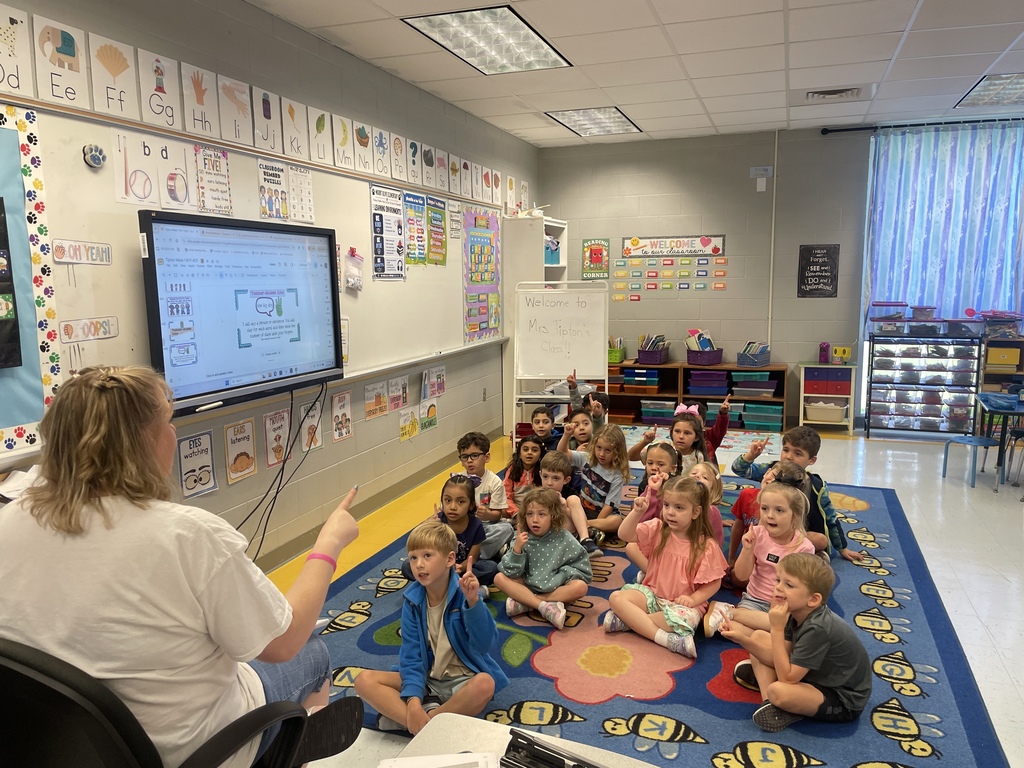 Teacher sitting with kindergarten class practicing a song.