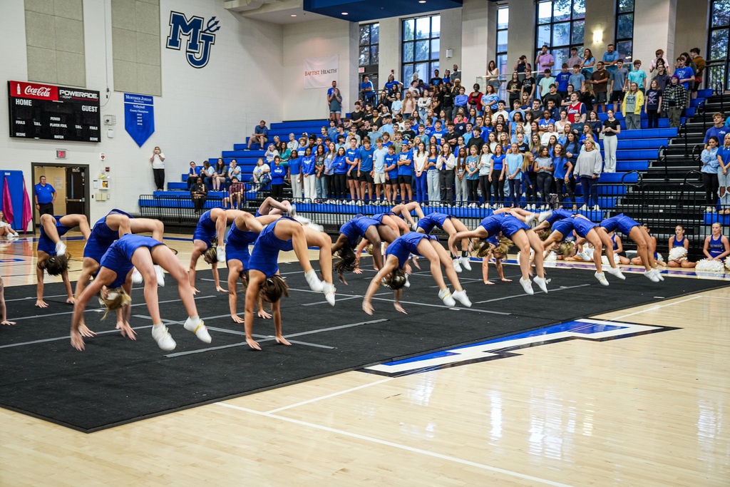 Cheerleaders do back hand springs during a pep rally in a school gym.