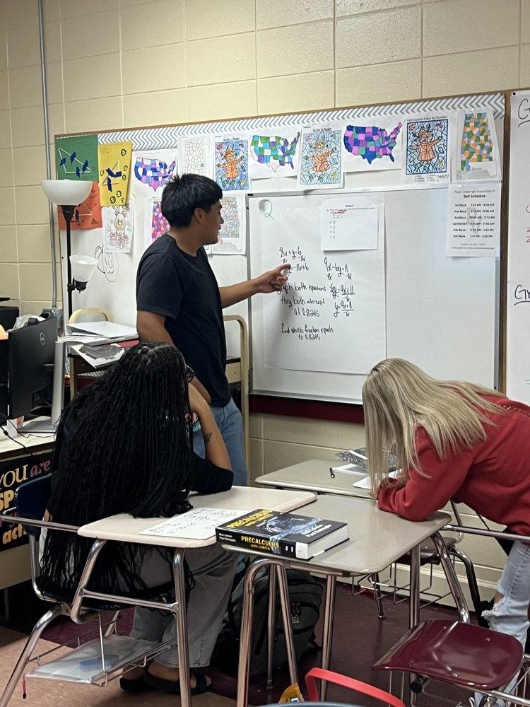 a student solves a math problem on a sheet of paper in front of their group