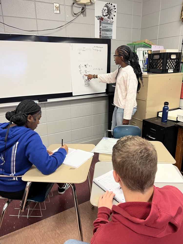 a student solves a math problem on a sheet of paper in front of their group