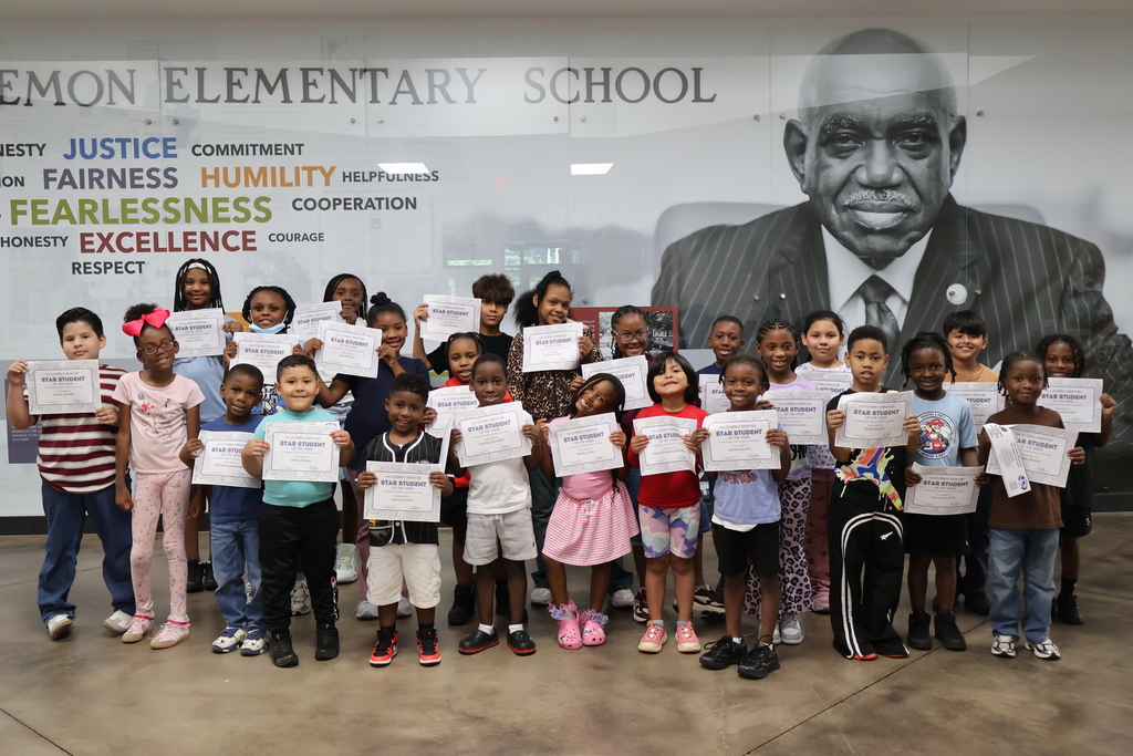 A group of students holding their "Student of the Month" certificates in front of the U.W. Clemon mural