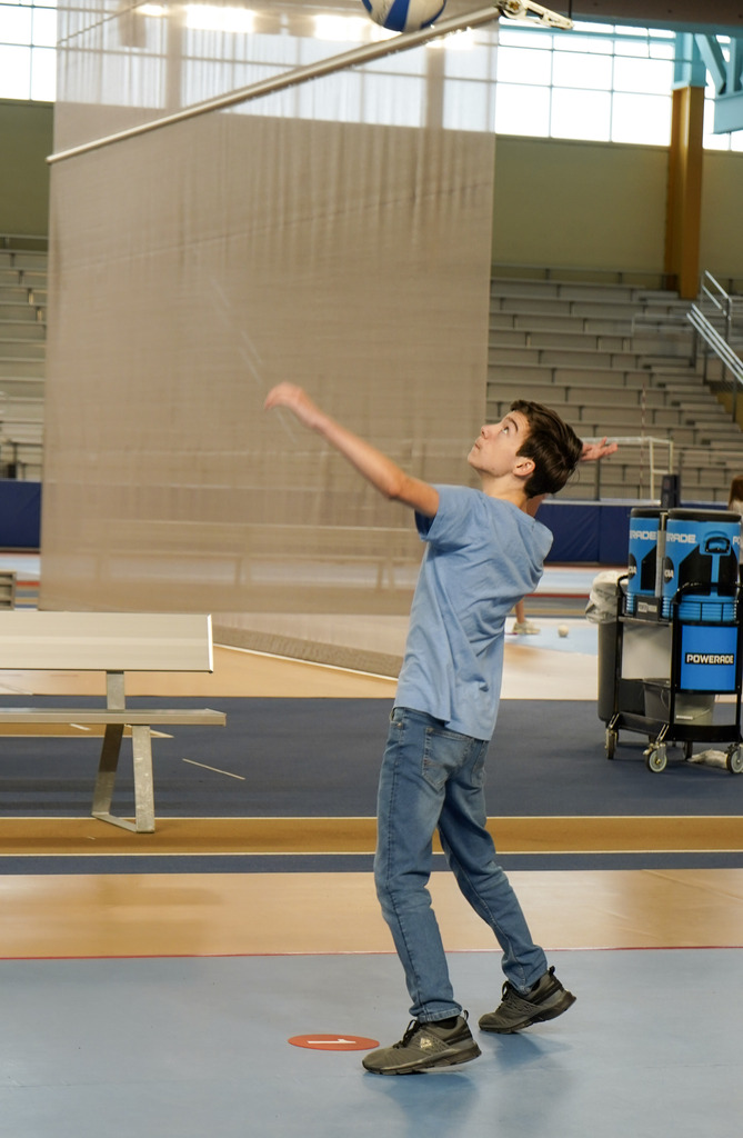 A student gets ready to serve a volleyball in a gymnasium.
