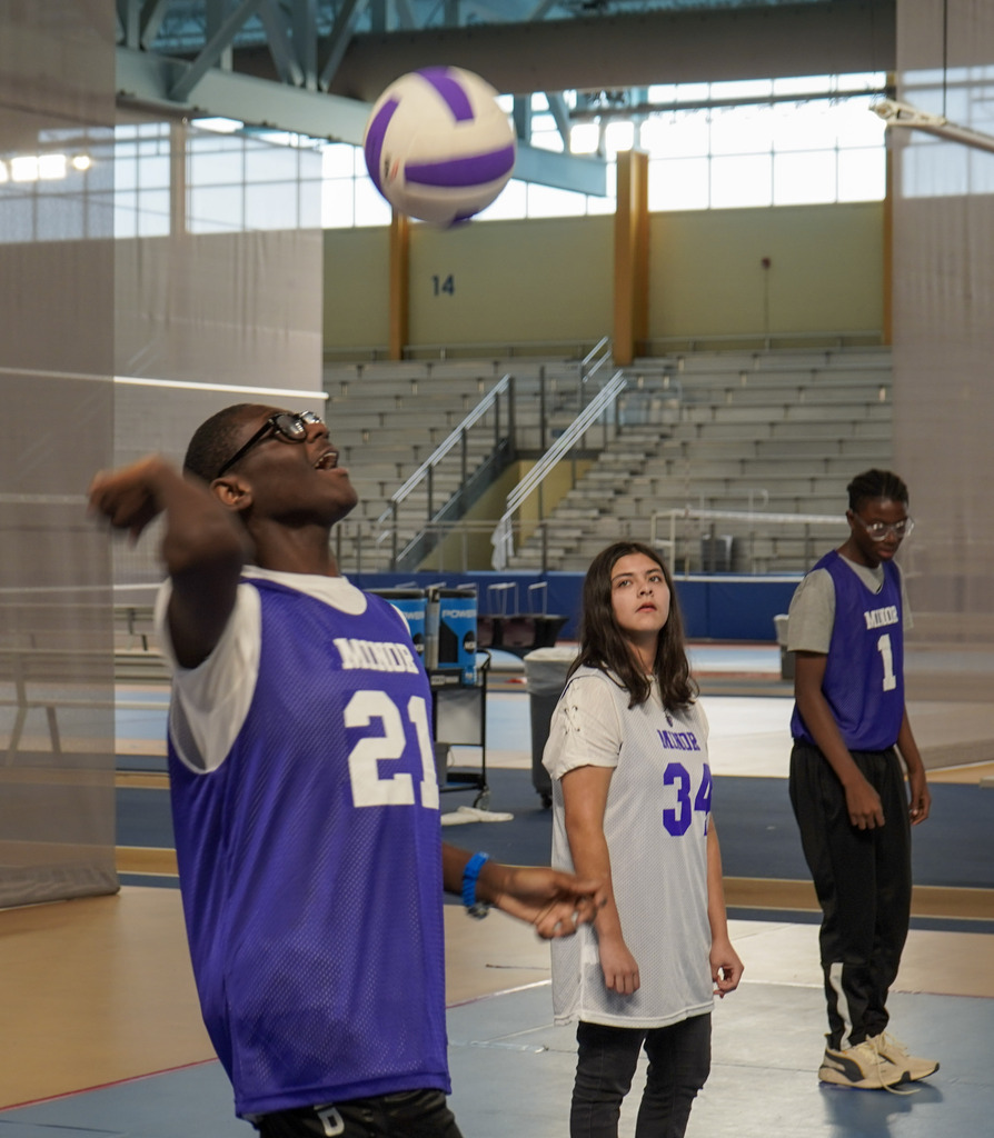 A student hits a volleyball inside a gym.