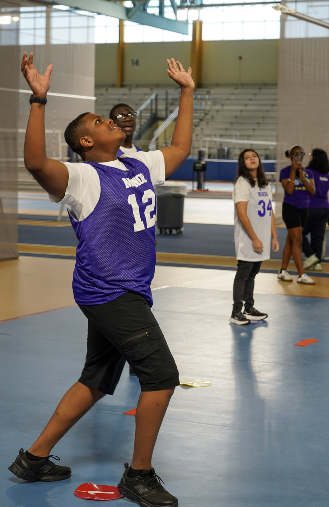 A student gets ready to hit a volleyball while standing in a gym.
