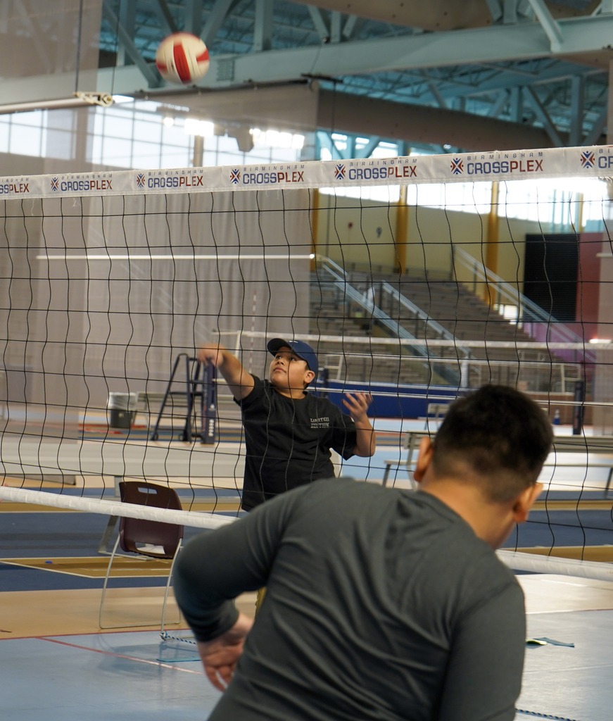 A student hits a volleyball over a net in a gym.