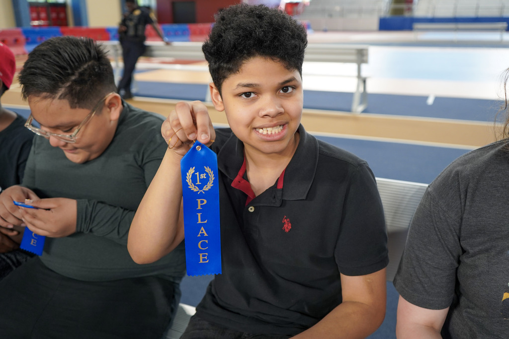 A student smiles while holding up a first place ribbon.