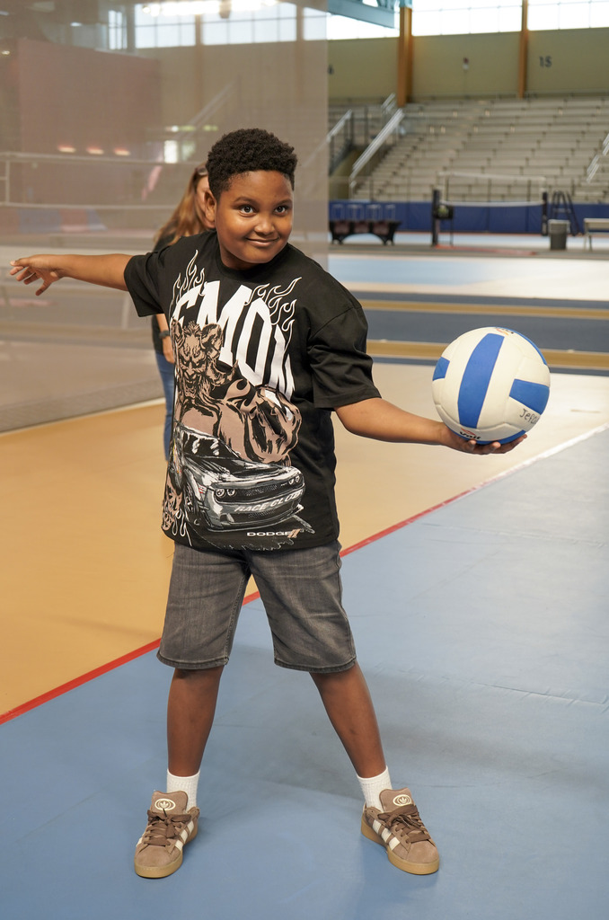A student gets ready to serve a volleyball while standing inside a gym.