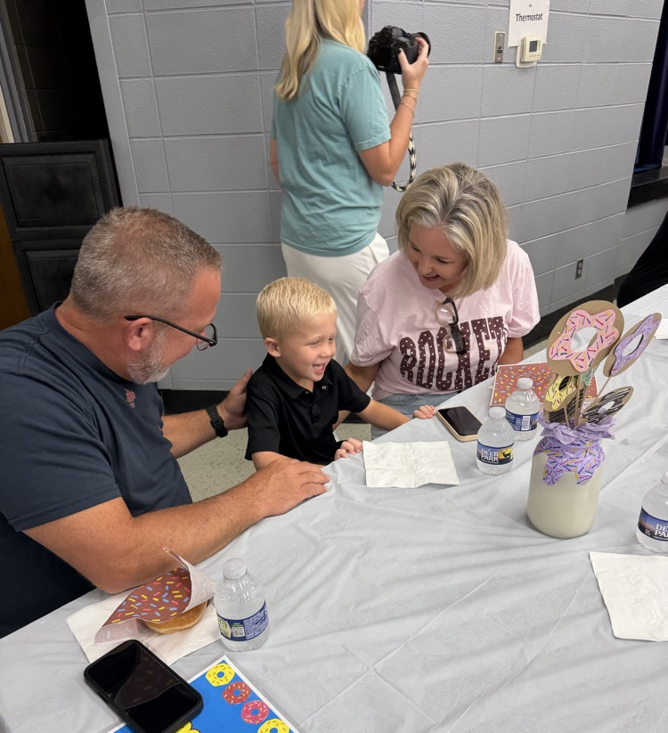 Two grandparents smiling and loving on a kindergarten boy
