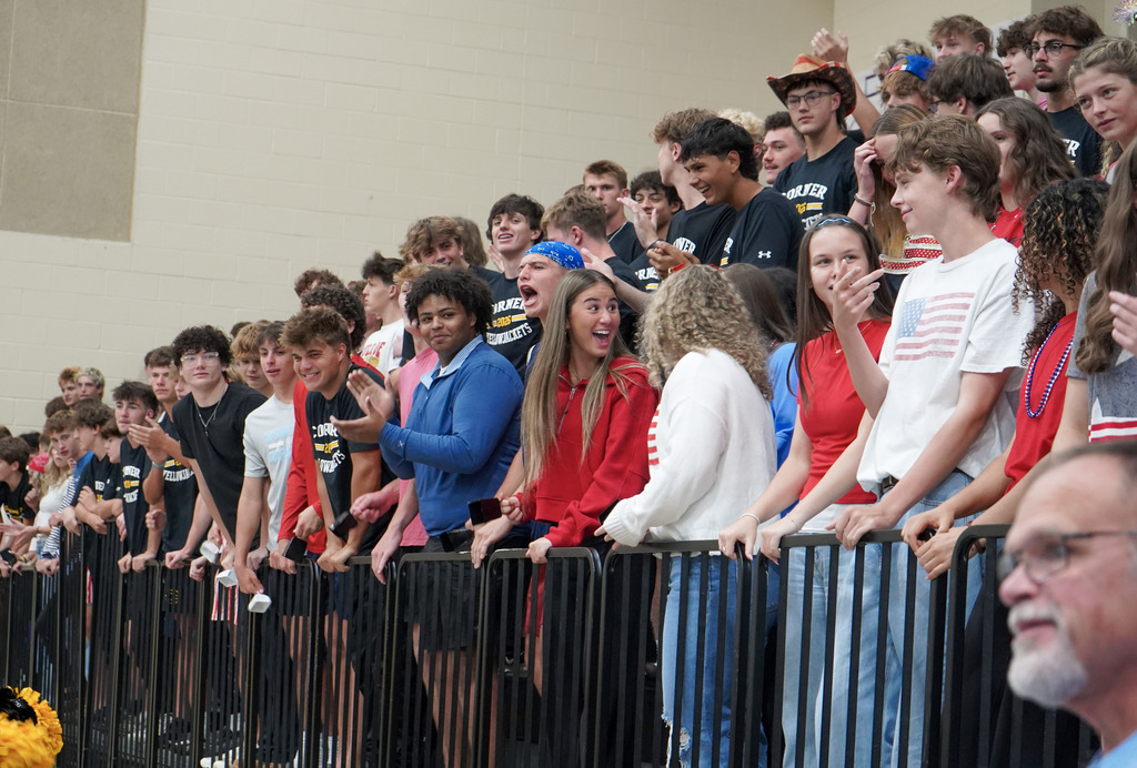 Students stand in bleachers and smile during a pep rally.