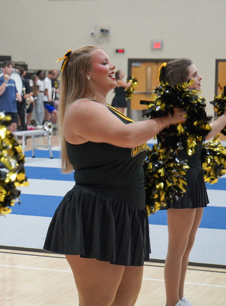 Students hold pom poms and dance during a pep rally.