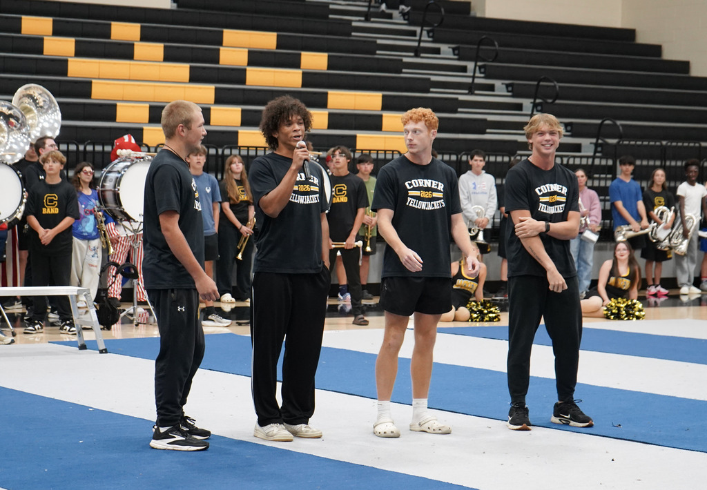 Students stand on a mat and speak into a microphone during a pep rally.