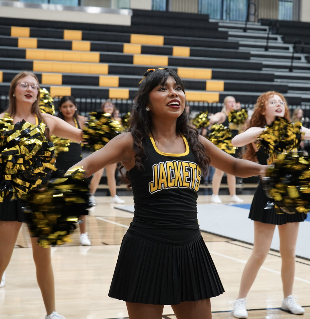 Students hold pom poms and perform a routine in a school gym.