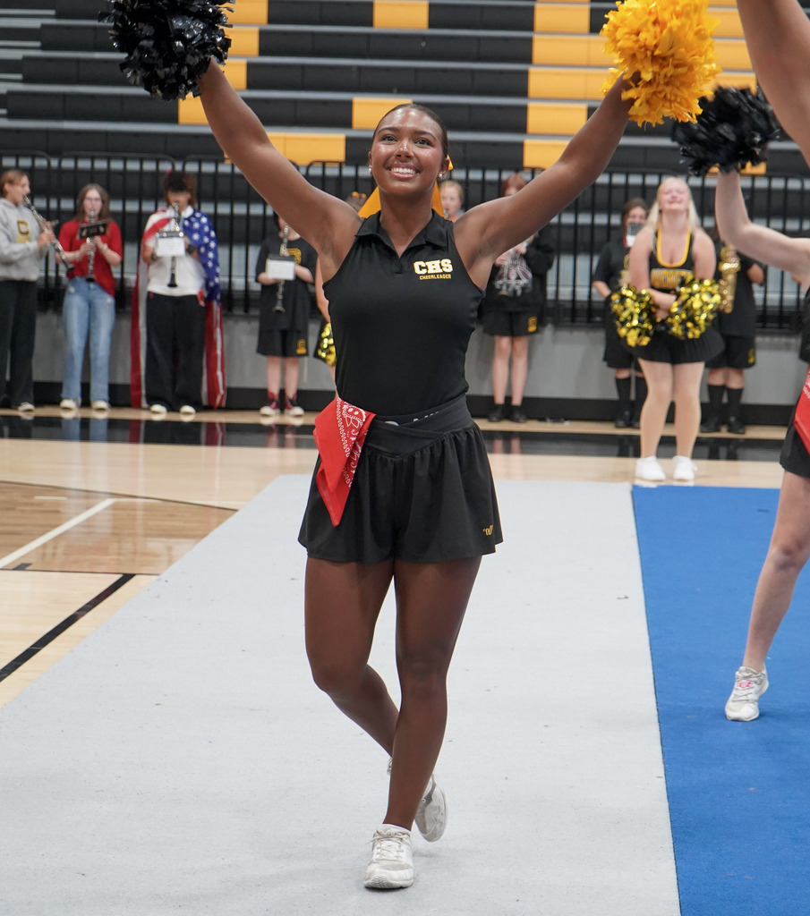 A cheerleader holds her hands in the air and smiles during a pep rally.