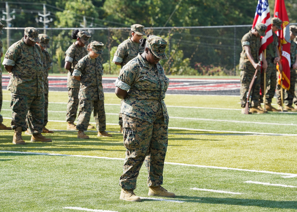 JROTC members stand with their heads bowed on a football field.