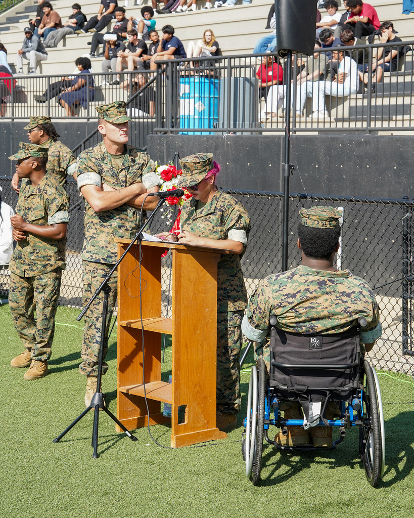 A student speaks into a microphone during a ceremony on a football field.