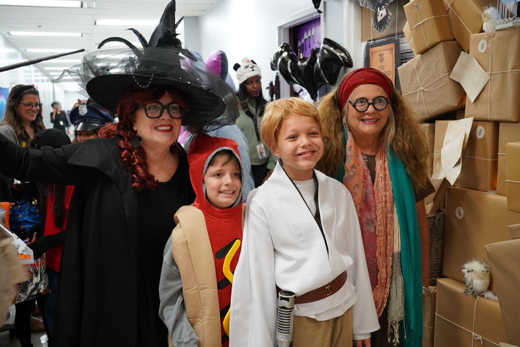 Students and adults are posing together in their halloween costumes. Left to right: witch, hot dog, Luke Skywalker, Harry Potter Character