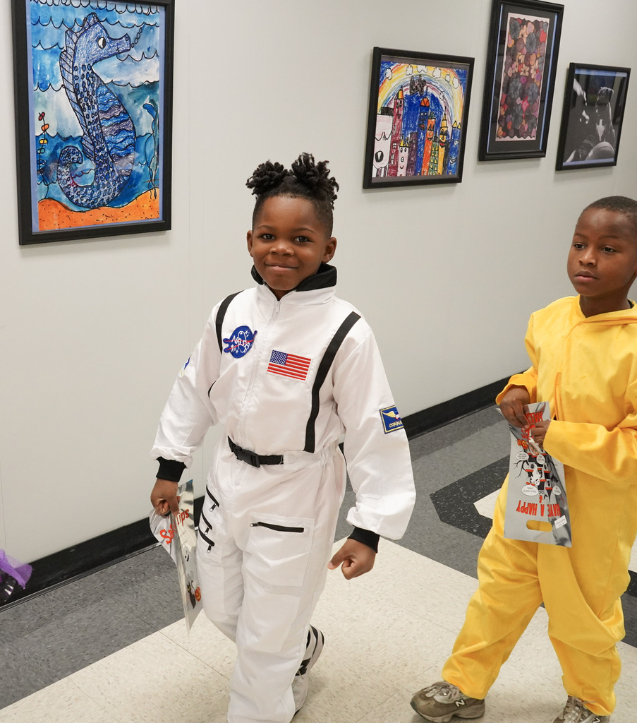 Children wearing Halloween costumes smile while walking through a hallway.