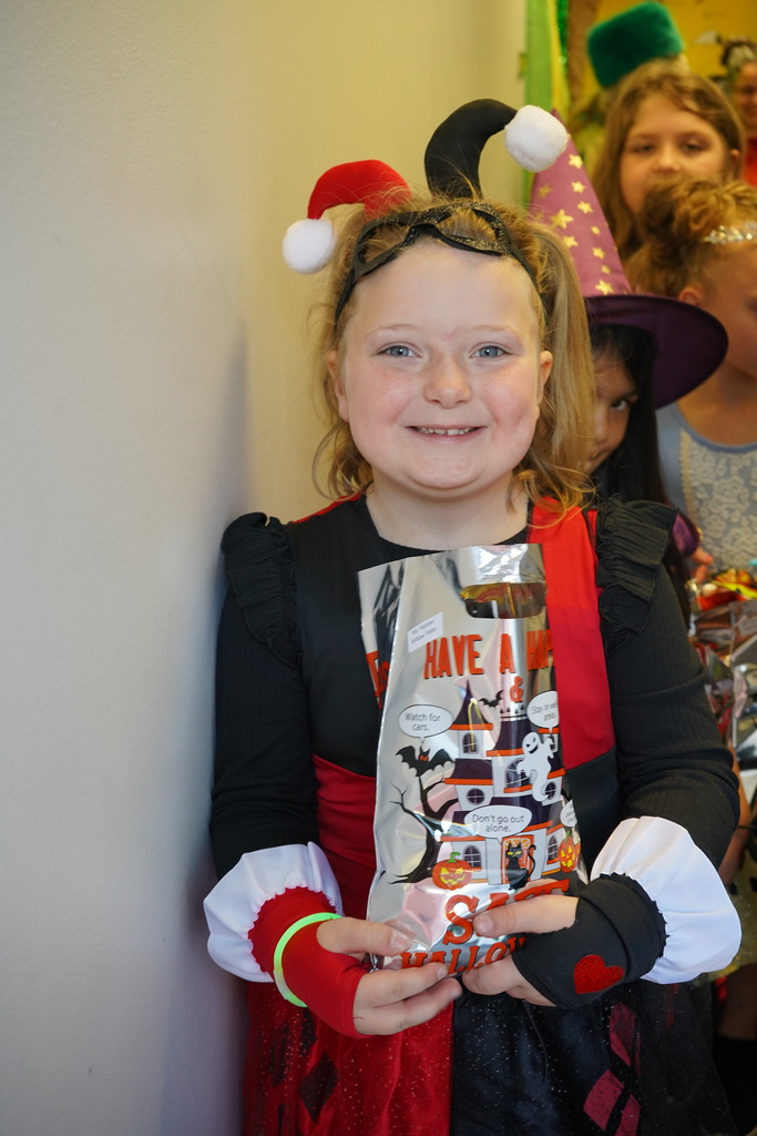 A student wearing a costume smiles for a photo while standing in a room and holding a bag of candy.