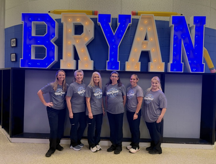 6 lunchroom ladies posing in front of the Bryan sign