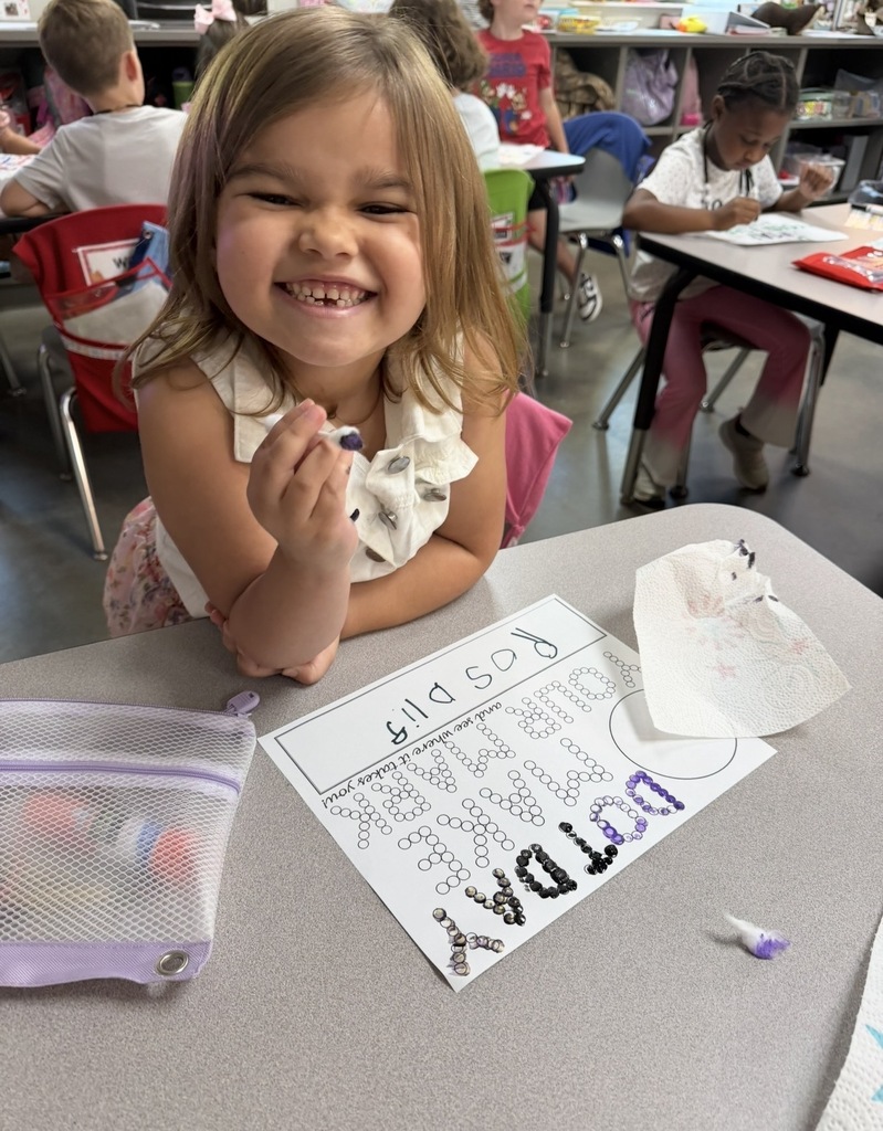 Student sitting at a desk painting a page that says "make your mark" using dots. The student is using a q tip and paint to paint the dots.