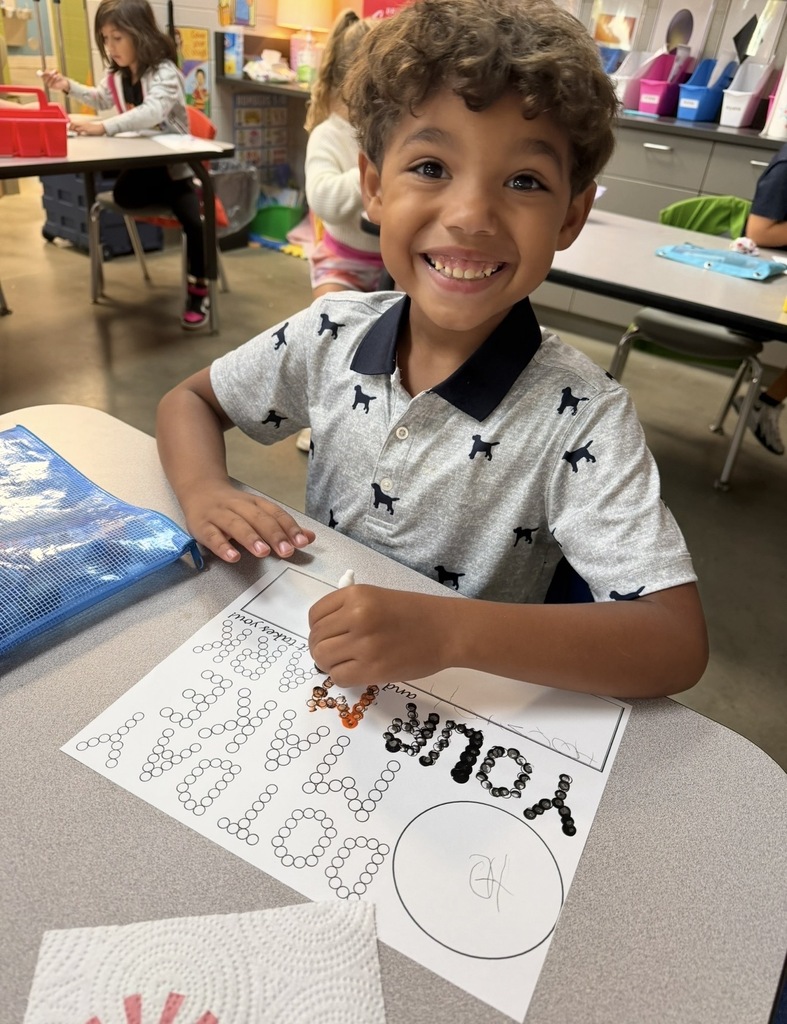 Student sitting at a desk painting a page that says "make your mark" using dots. The student is using a q tip and paint to paint the dots.