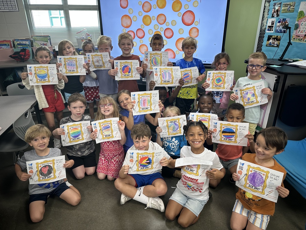 Students are posing together holding up their art work where they colored their own dots.