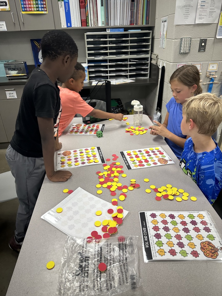 4 students are at a table together playing a game with red and yellow dot counters and a game board.
