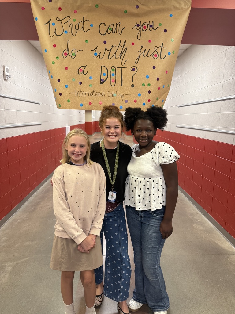 Teacher and two students posing under a sign that says "what can you do with just a dot?" in polka dot clothing.