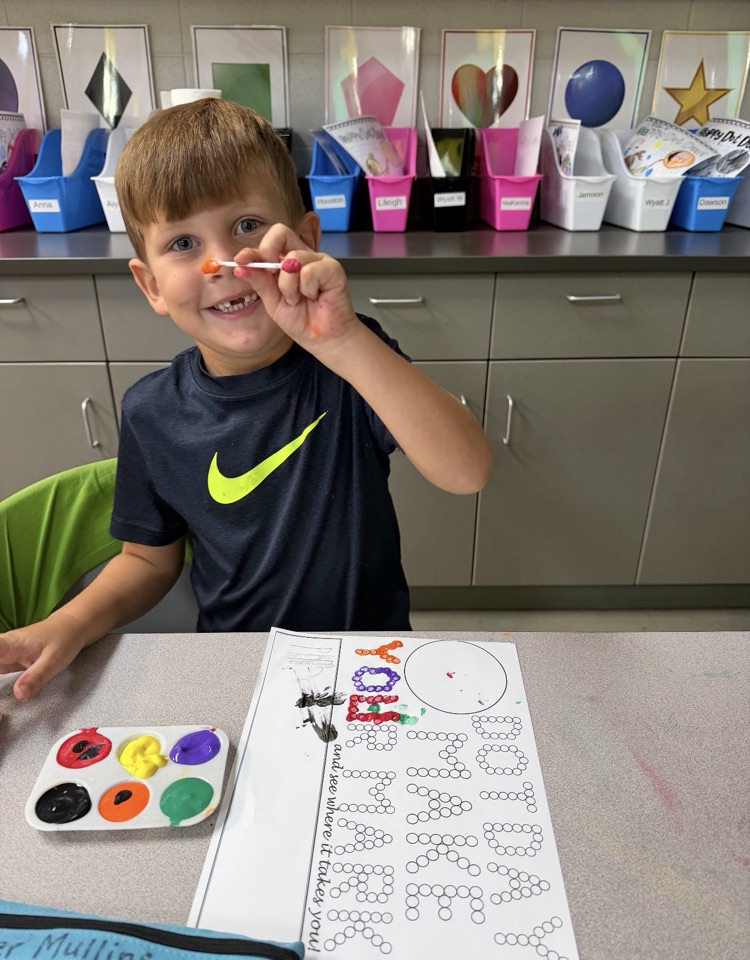 student painting a page that says “make your mark” with q tips holding the q tip with paint up to the camera