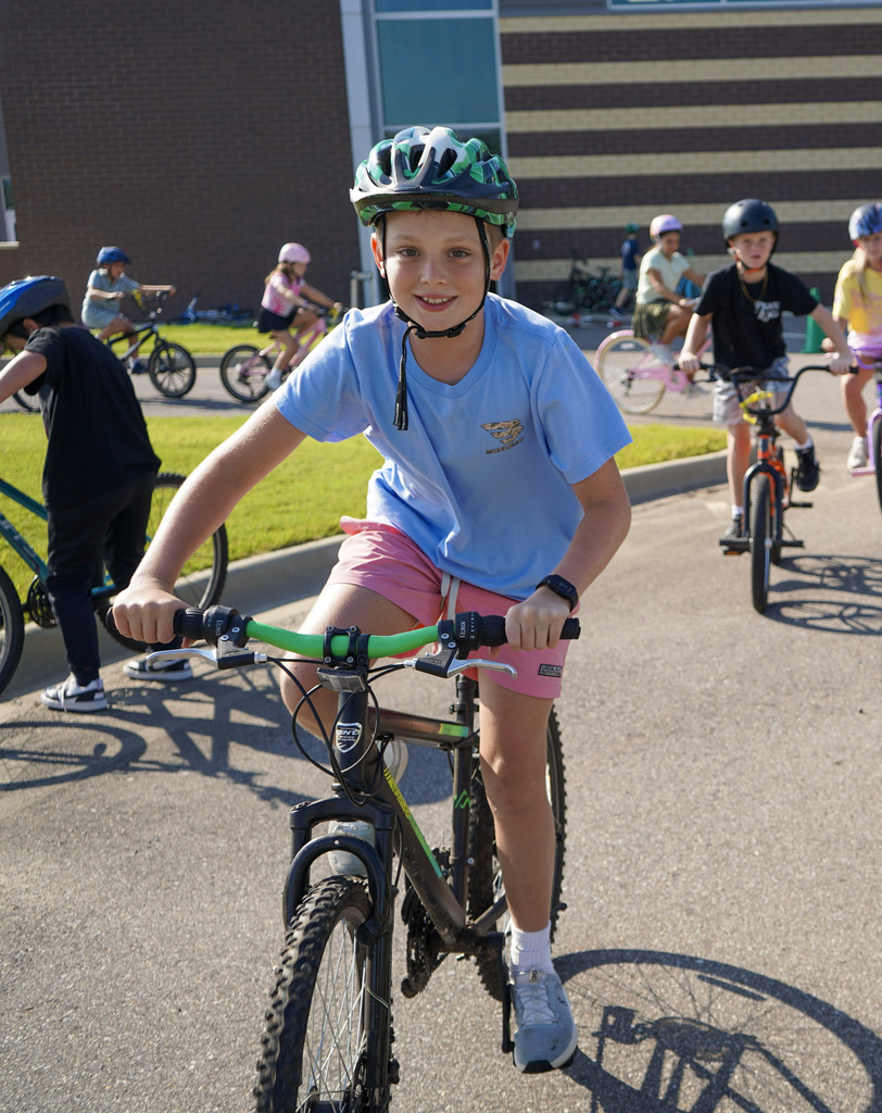 A child smiles while riding a bike outside a school.