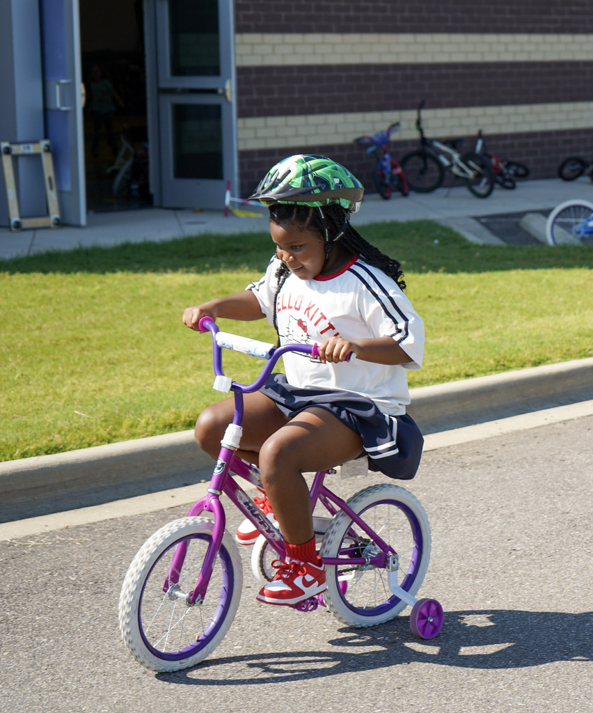 A student smiles while riding a bike outdoors.