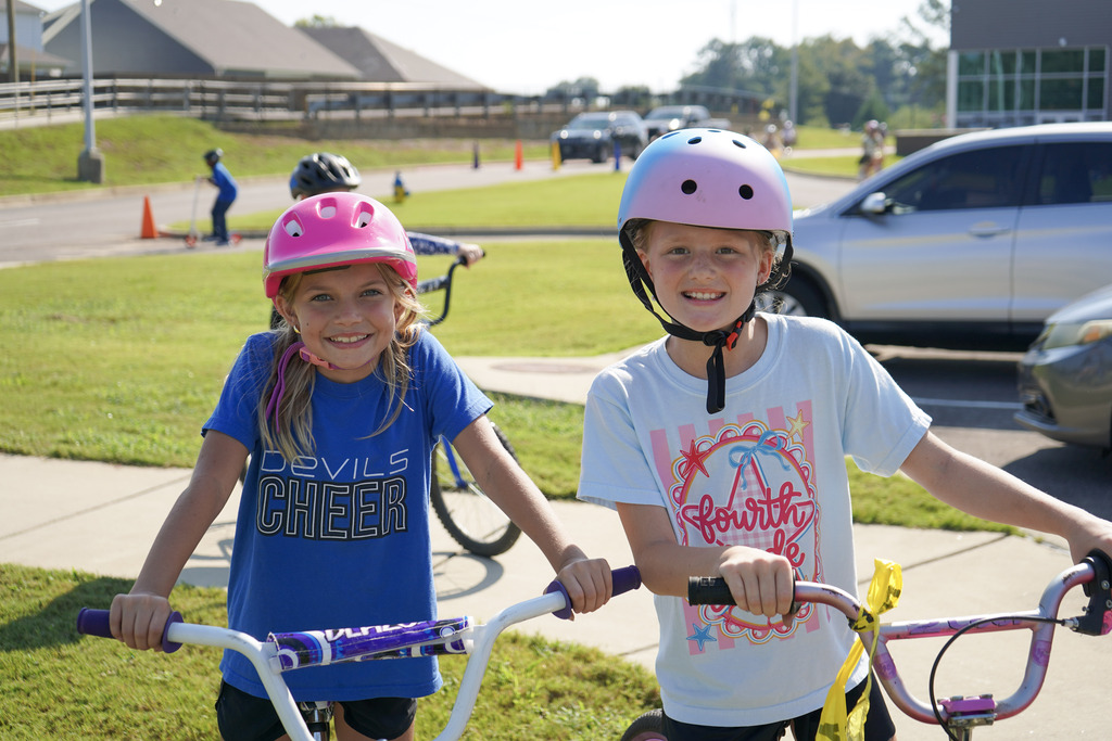 Two students hold bicycles and smile for a photo while standing outdoors.