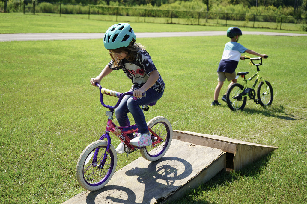 A girl smiles while riding a bike over a ramp outdoors.
