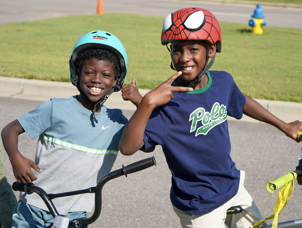Two students smile while standing behind bikes outdoors.