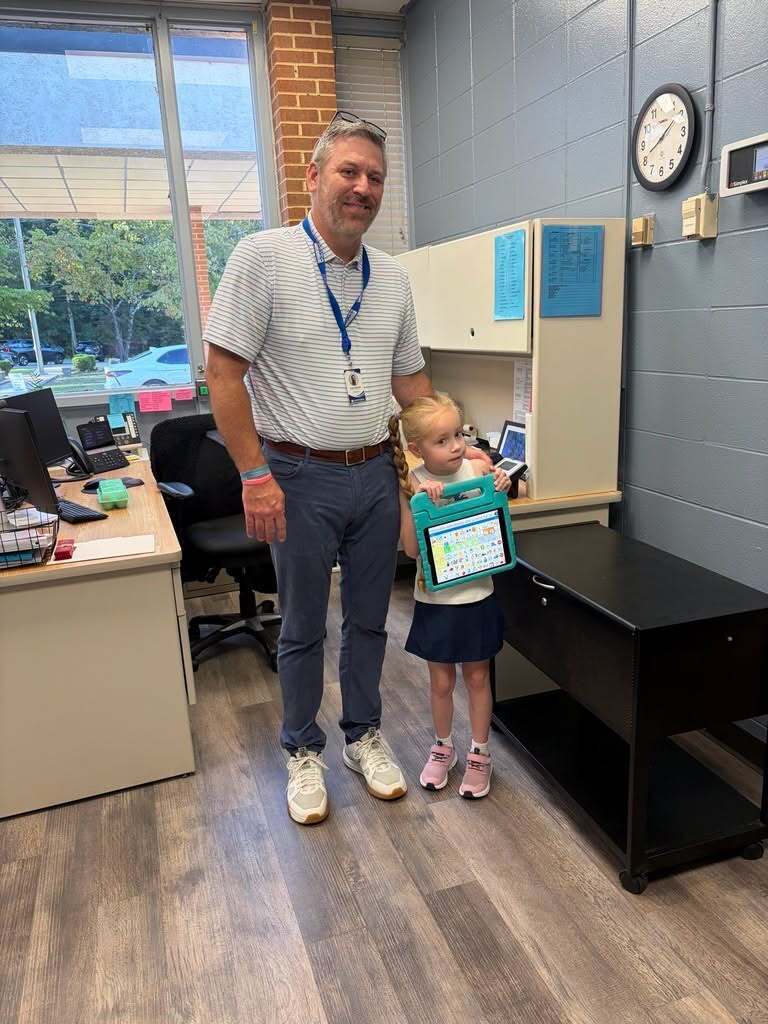A child and a man smile for a photo inside a school office.