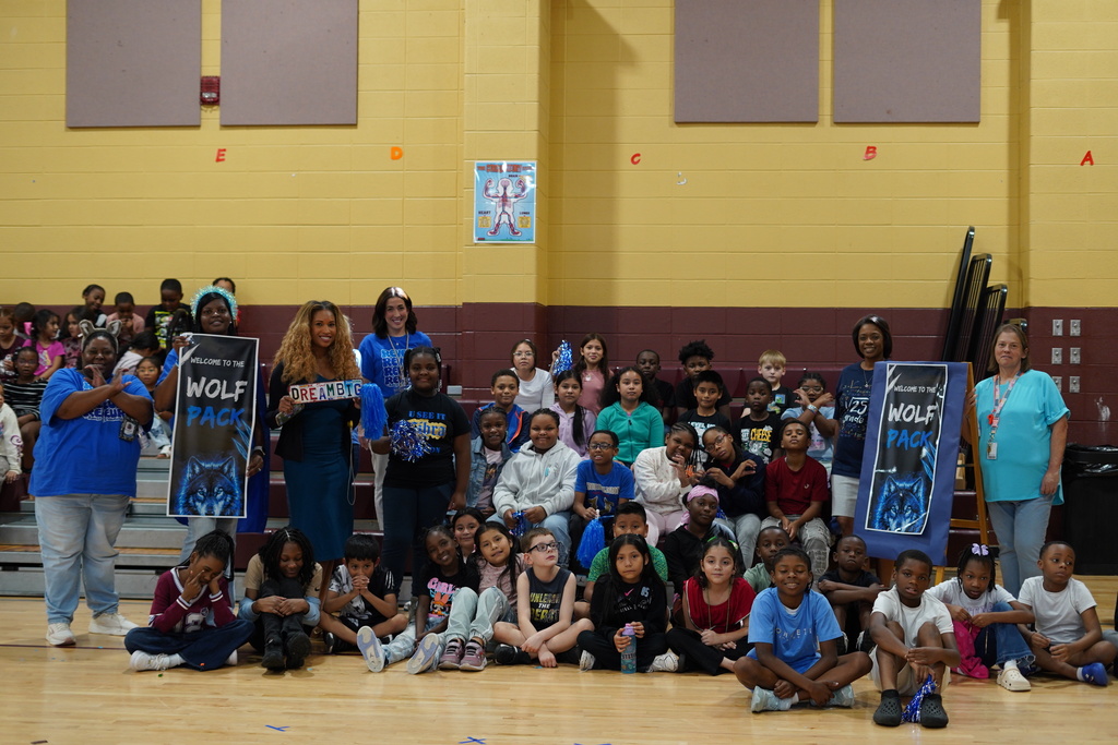 Students and teachers smile for a photo in a school gym.