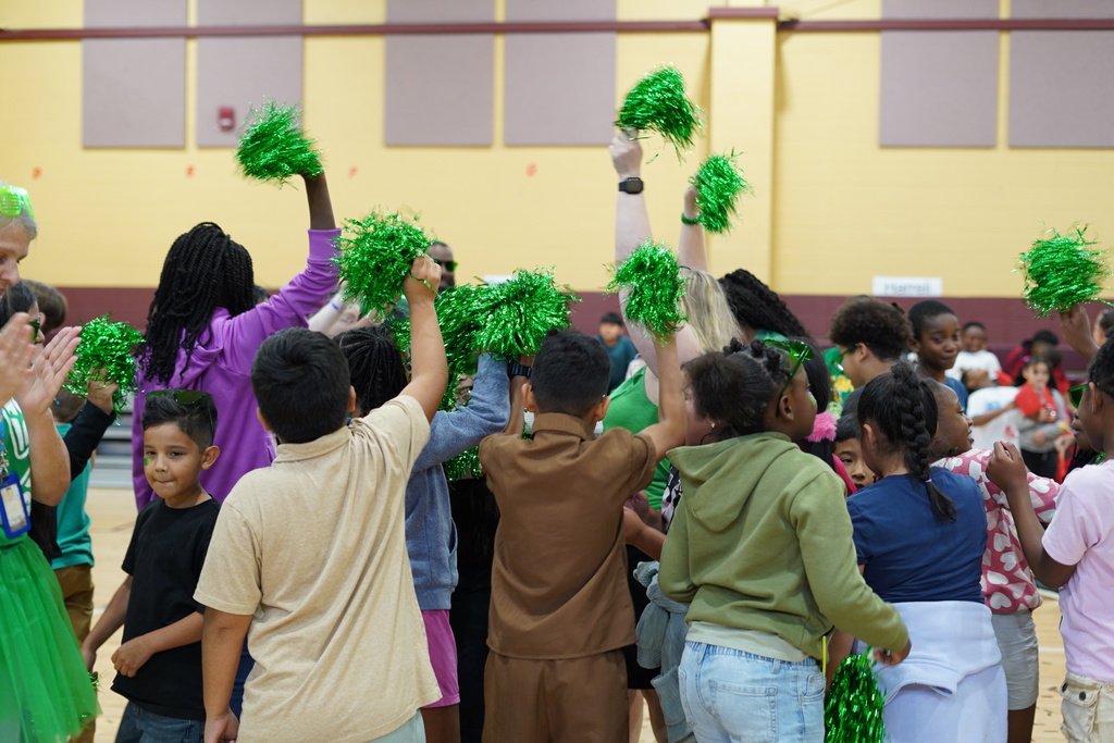 Students shake green shakers while standing in a school gym.