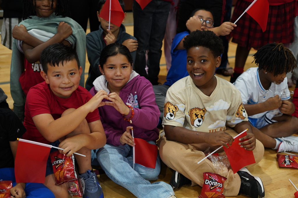 Students hold red flags and smile for a photo in a school gym.