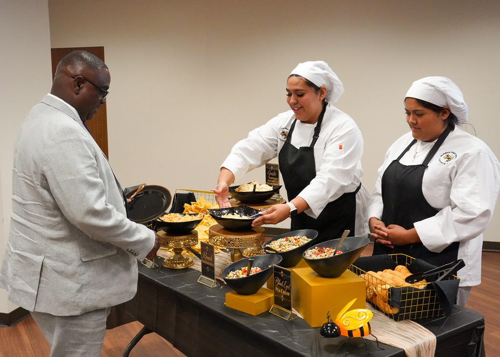 Two students from McAdory high school's culinary arts program are serving Dr. Walter Gonsoulin during Mr. Bobby Jackson's retirement party.