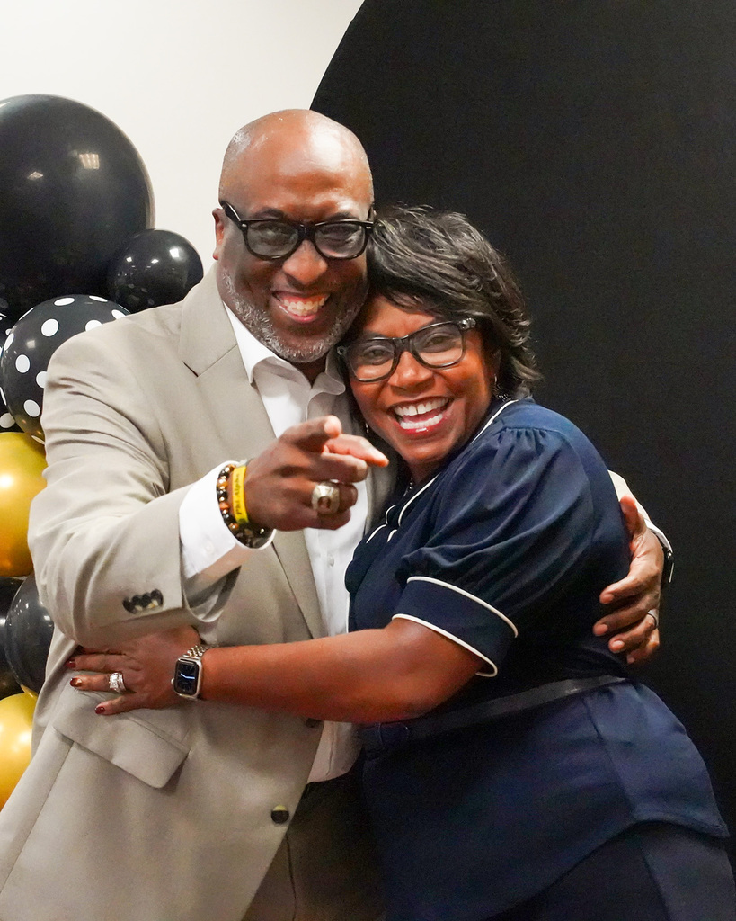Mr. Bobby Jackson points at the camera and smiles while hugging a colleague during his retirement party.